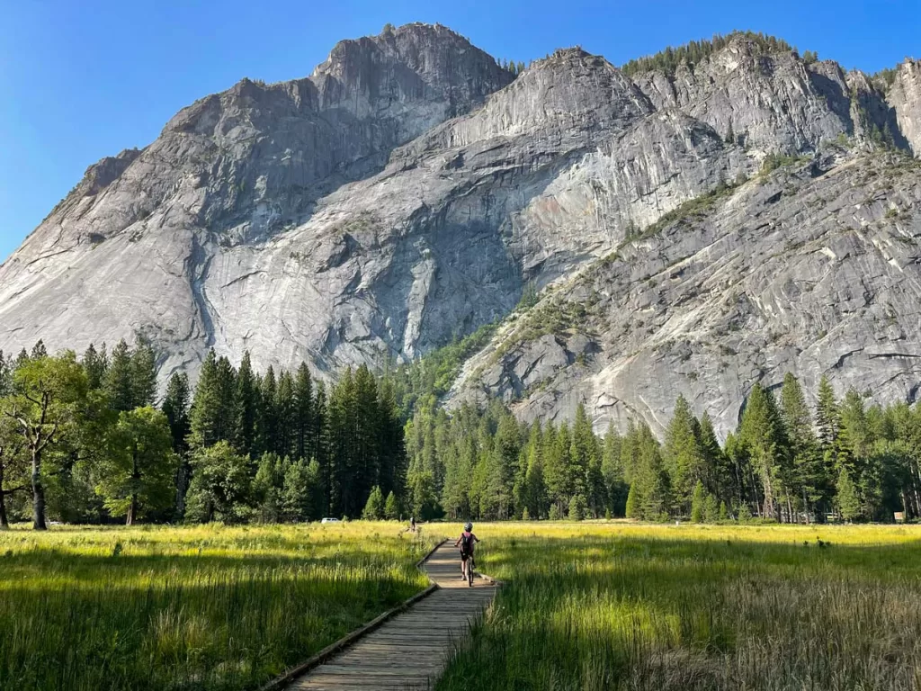 A child bikes along a wooden boardwalk through a meadow in Yosemite National Park.