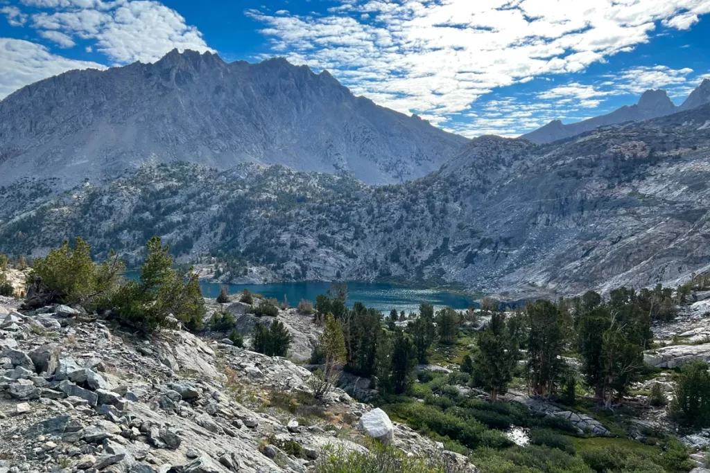 The summit of Glen Pass along the Rae Lakes Loop looks down on a sparkling high alpine lake, surrounded by granite peaks and small pine trees.