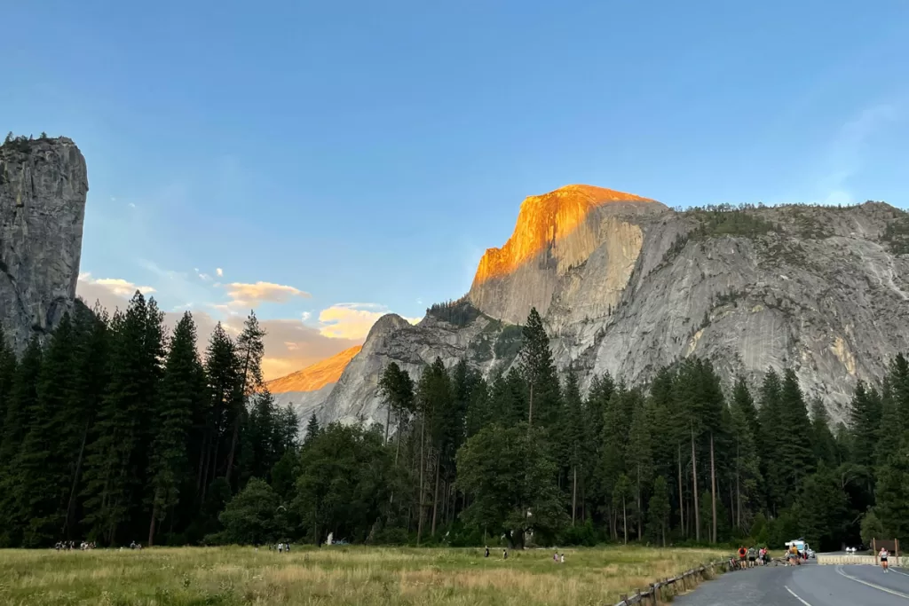 Evening alpenglow falls across the granite face of Half Dome in Yosemite National Park on a summer night.