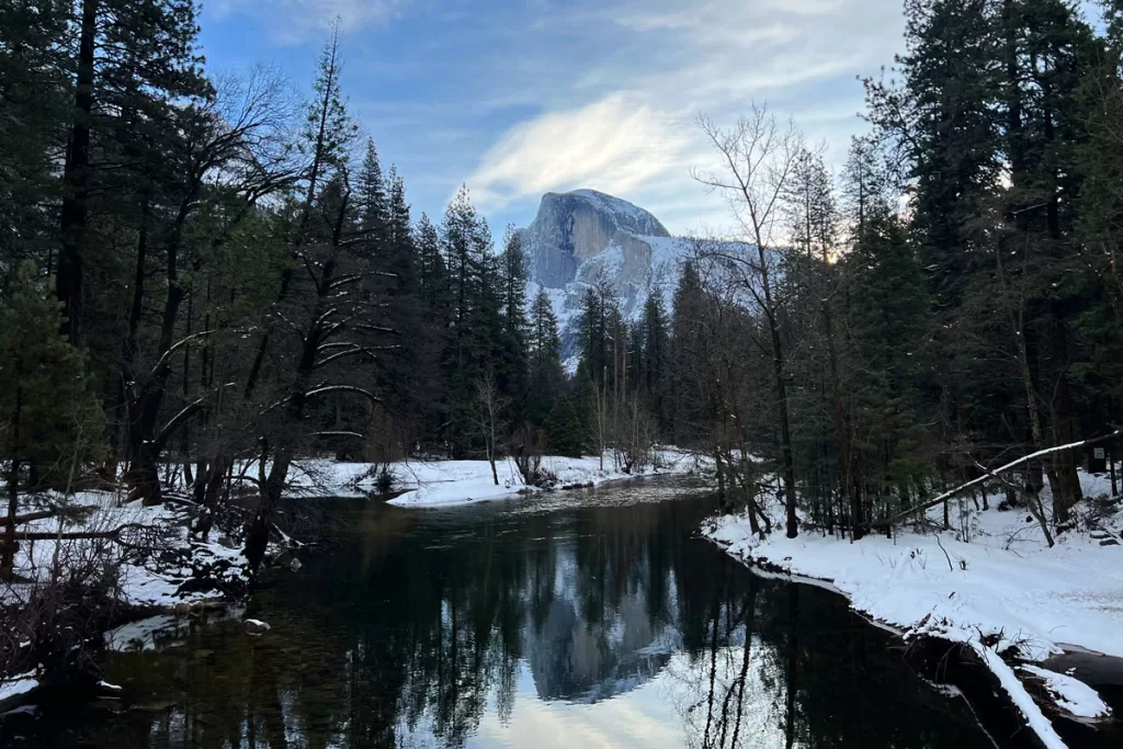 Yosemite's iconic Half Dome, dusted in snow, is reflected in the still waters of the Merced River on a winter day.