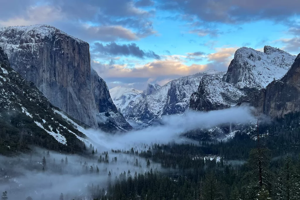 Mist and low clouds settle over Yosemite Valley during a winter sunset, with El Capitan and surrounding peaks dusted in snow.