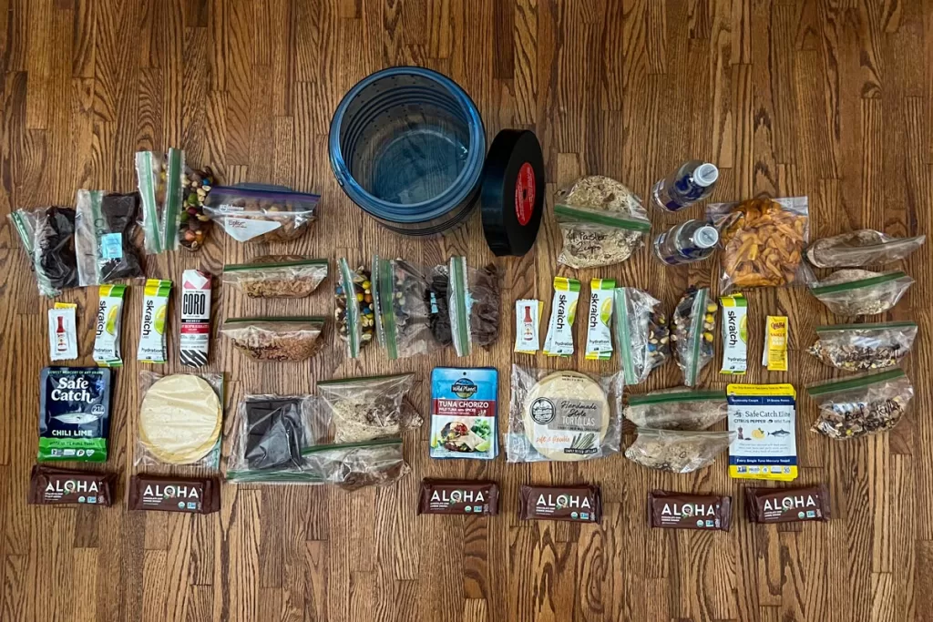 An overhead view of pre-portioned backpacking food ideas, laid out on a wood floor.