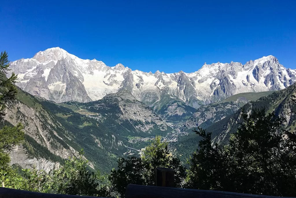 Snowcapped peaks of the Col d'Arpy rise above a green valley near Mont Blanc in Aosta Valley, Italy.