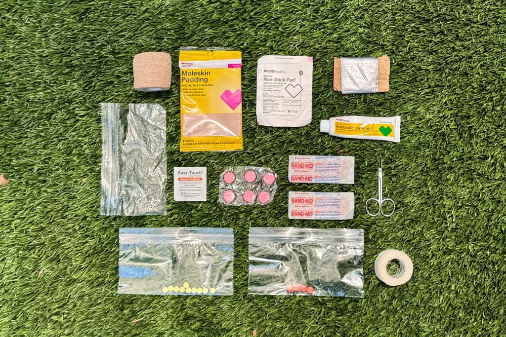 Items that make up a backpacking first aid kit are organized on grass.