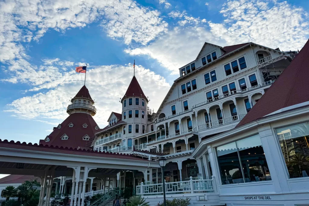 An angled image looking up towards the iconic red tower and Victorian facade of the Hotel Del in Coronado, California.