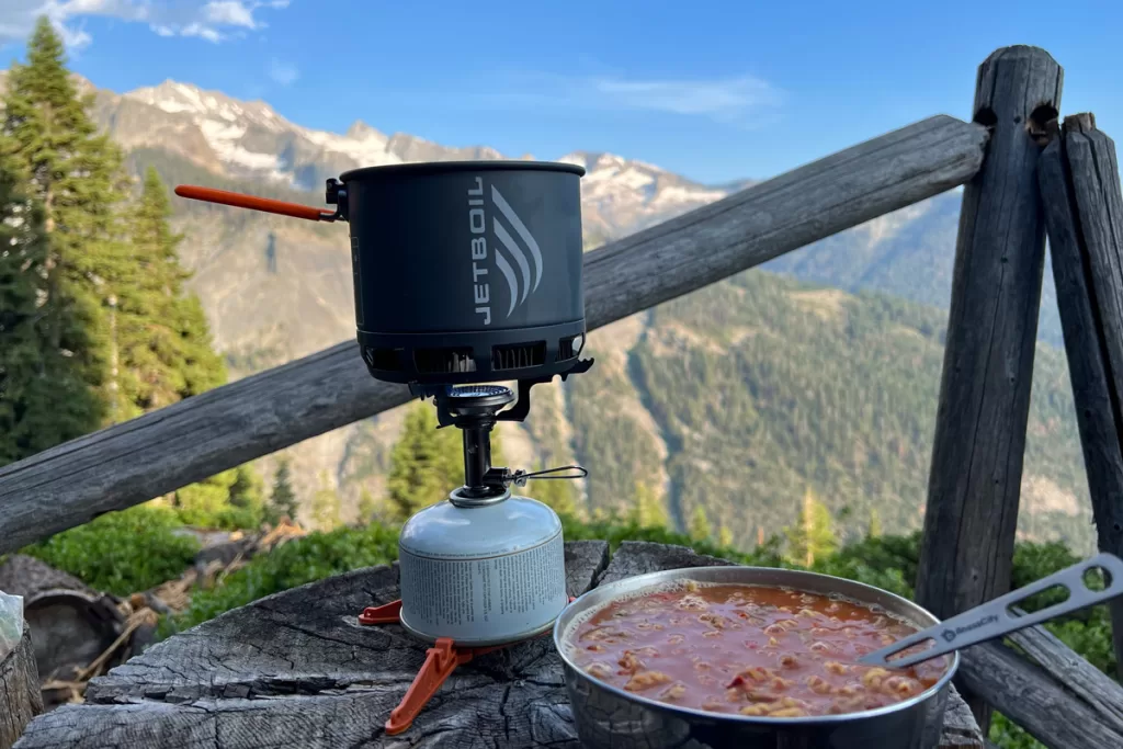 A bowl of chili sits next to a Jetboil backpacking stove against a mountainous backdrop.