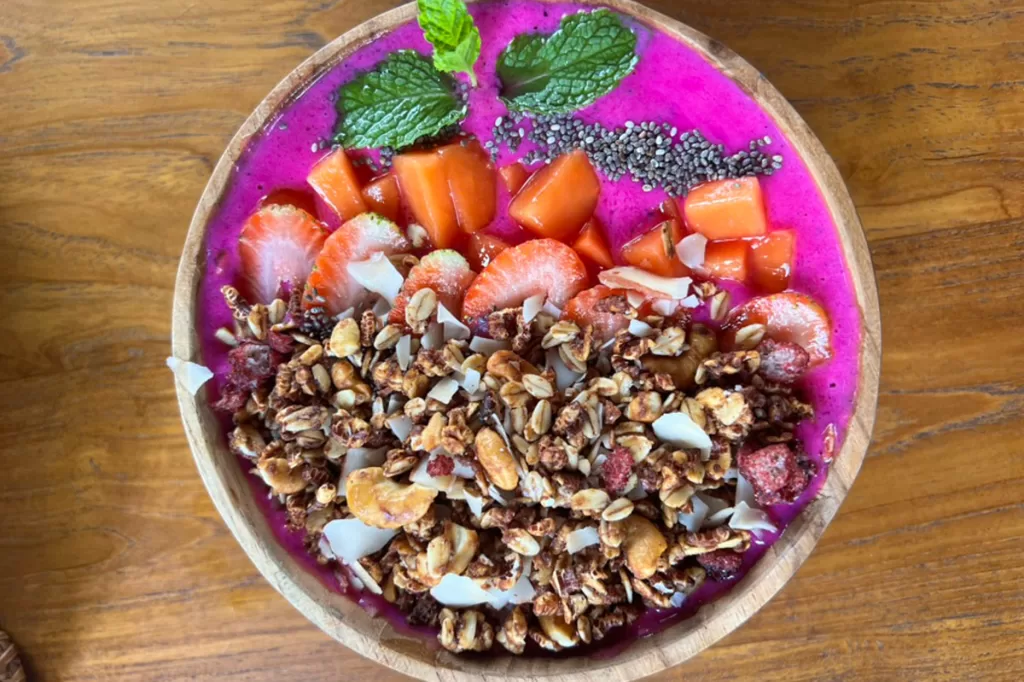 A brightly colored acai bowl, with granola, fresh fruit, chia seeds, and mint garnish.