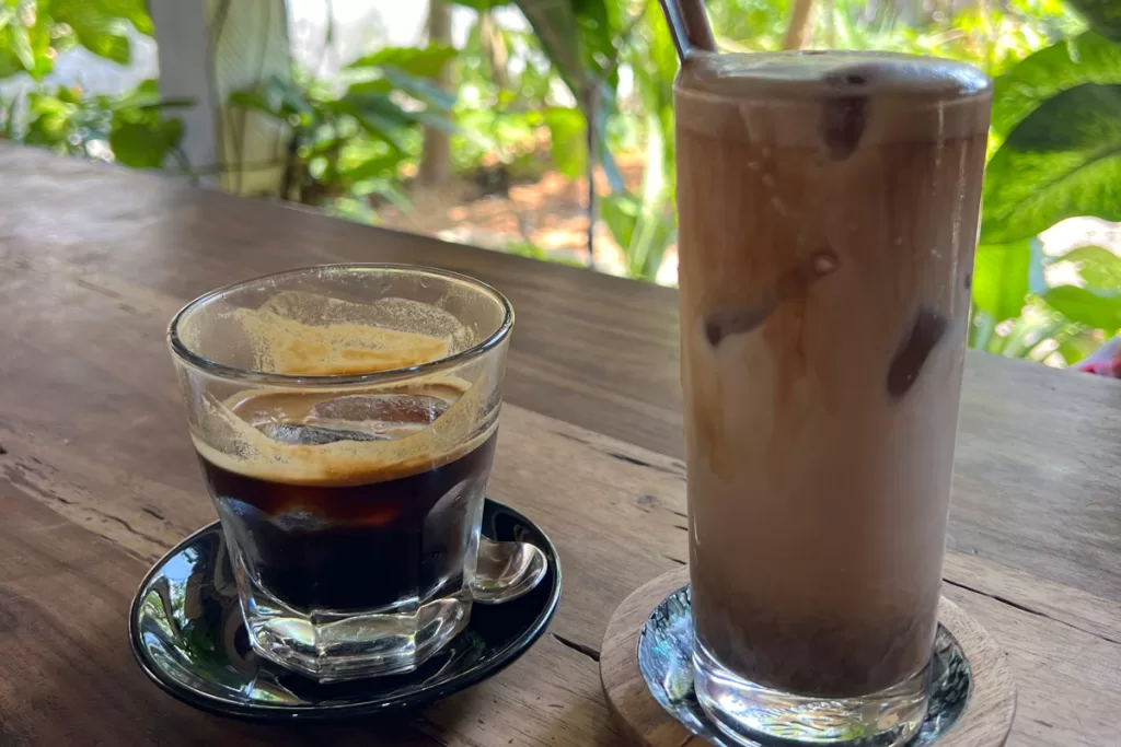 Two coffee drinks sit on a wooden table surrounded by palms at Gili Coffee Roasters on Gili Air, Indonesia.