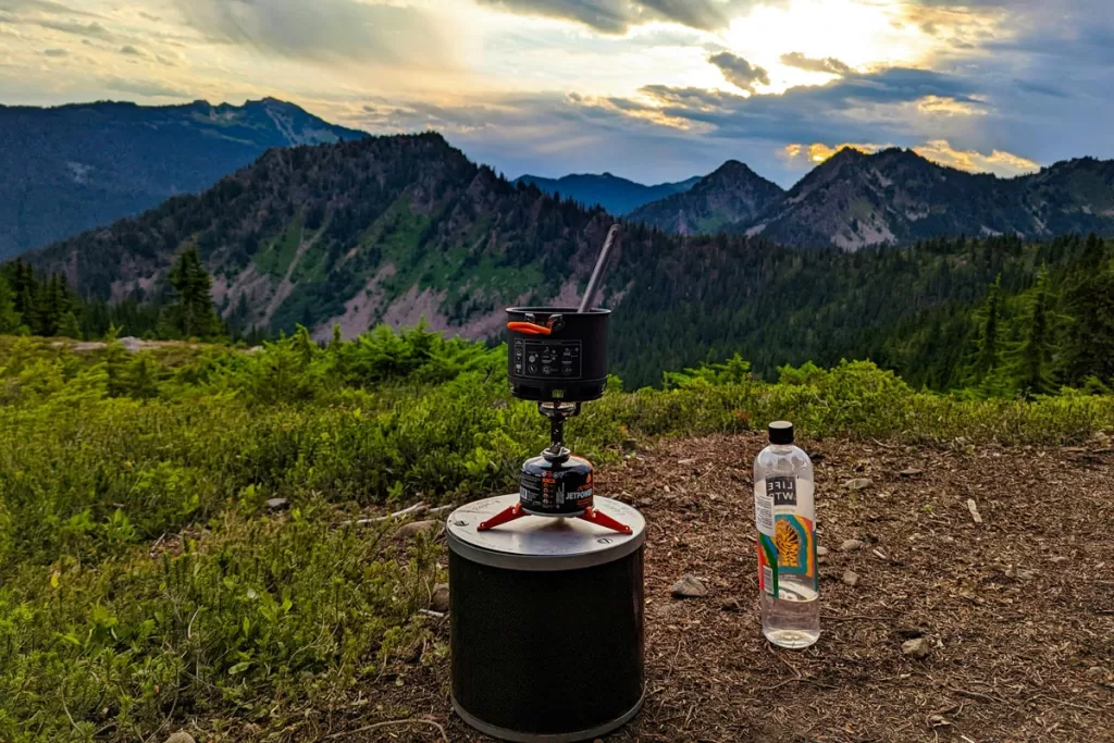 A JetBoil camping stove sits on a ridge above forested mountain peaks.