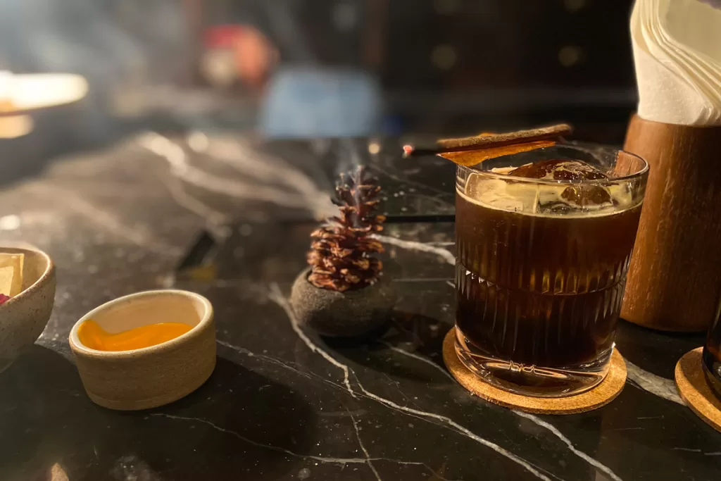 A craft cocktail, complete with smoked pinecone, sits on a black marble counter at Night Rooster cocktail bar in Ubud, Bali, Indonesia.