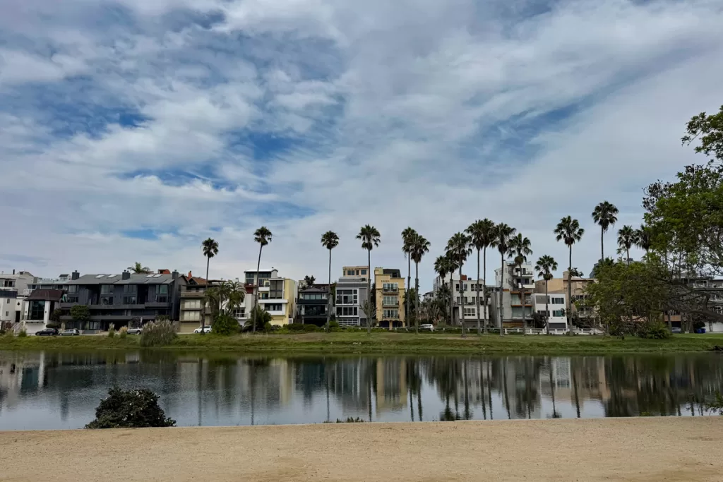 Homes and palm trees line the grassy shoreline and are reflected in the calm waters of Playa del Rey lagoon in Los Angeles, California.