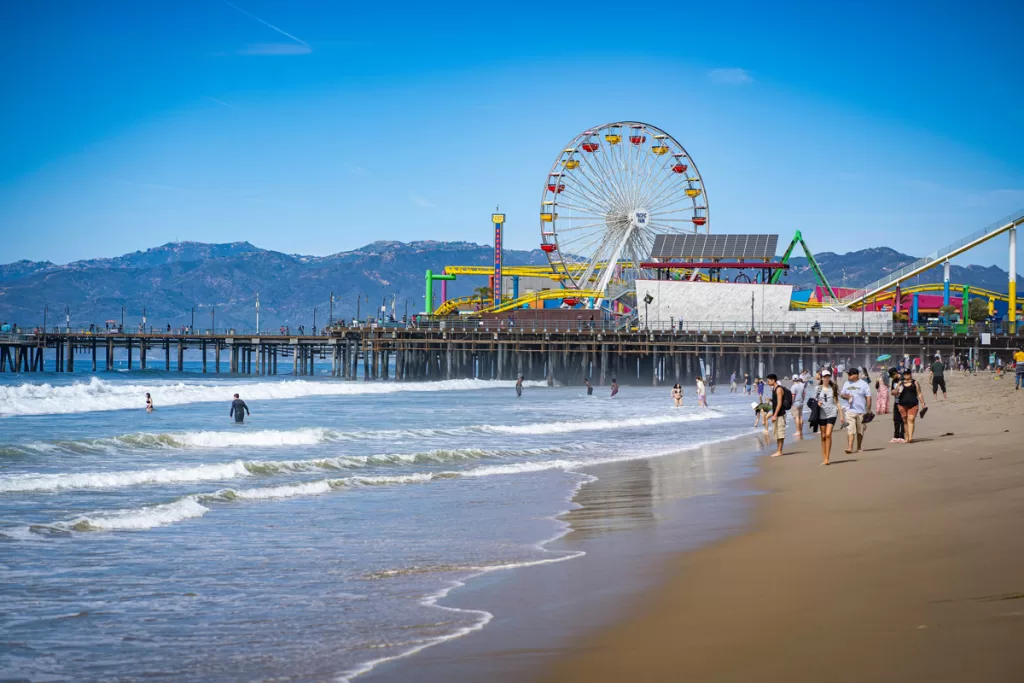 People walk along the beach in front of Santa Monica Pier in Los Angeles, California