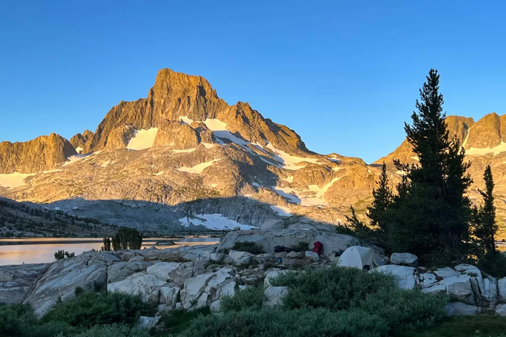 Dawn alpenglow hits Mount Banner overlooking Thousand Island Lake in the eastern Sierra Nevada mountains, with a small campsite in shadow in the foreground.