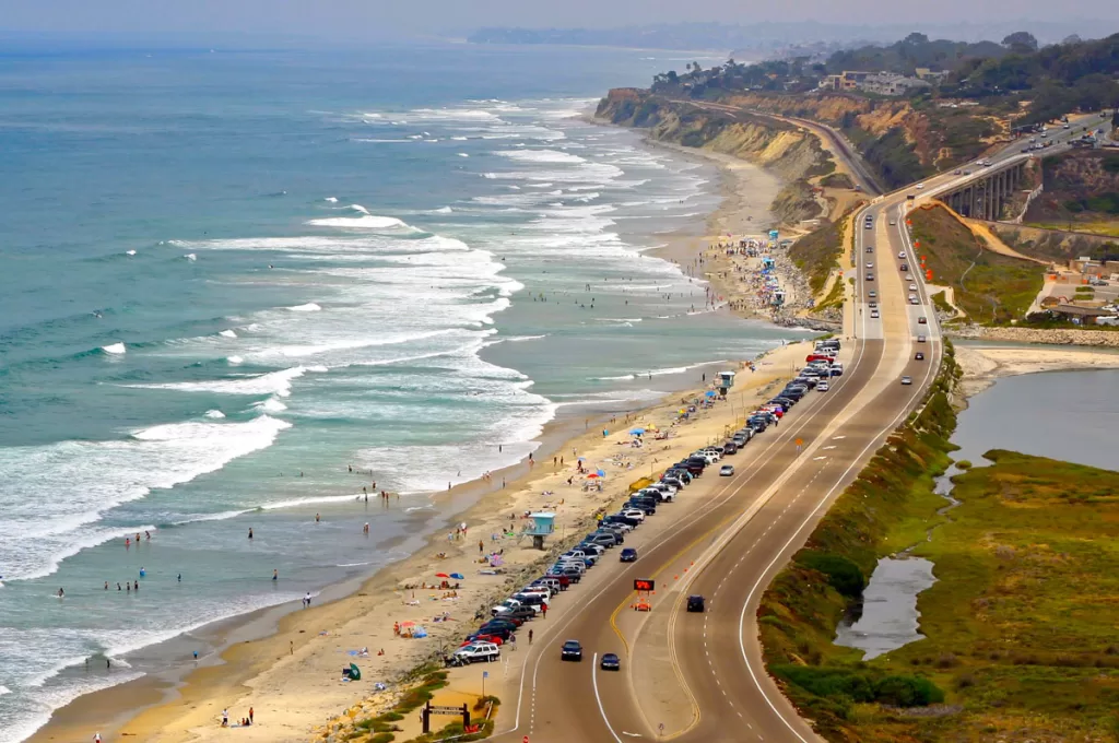 A bird's eye view of Torrey Pines State Beach shows cars parked along the road stretching up to the bluffs of Del Mar, California.