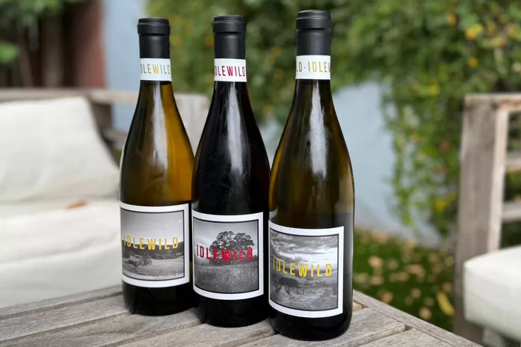 Three bottles of wine from Idlewild Winery in Healdsburg, California sit on a wooden table.