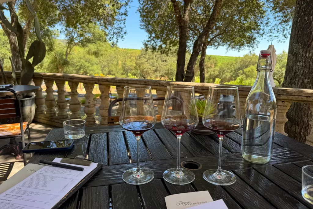 Three wine glasses on a table overlooking the vineyard at Reeve Winery near Healdsburg, California.