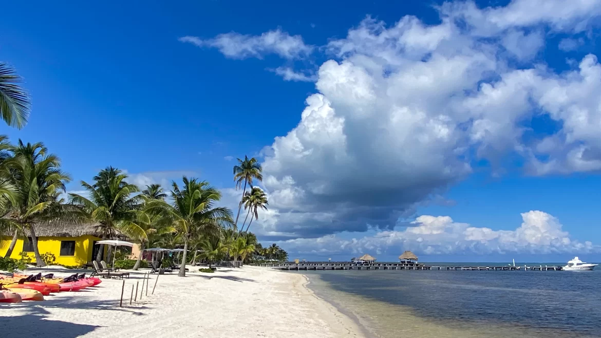 Belize_Feature A white sand beach is lined with palm trees and colorful thatched huts in Ambergis Caye, Belize.