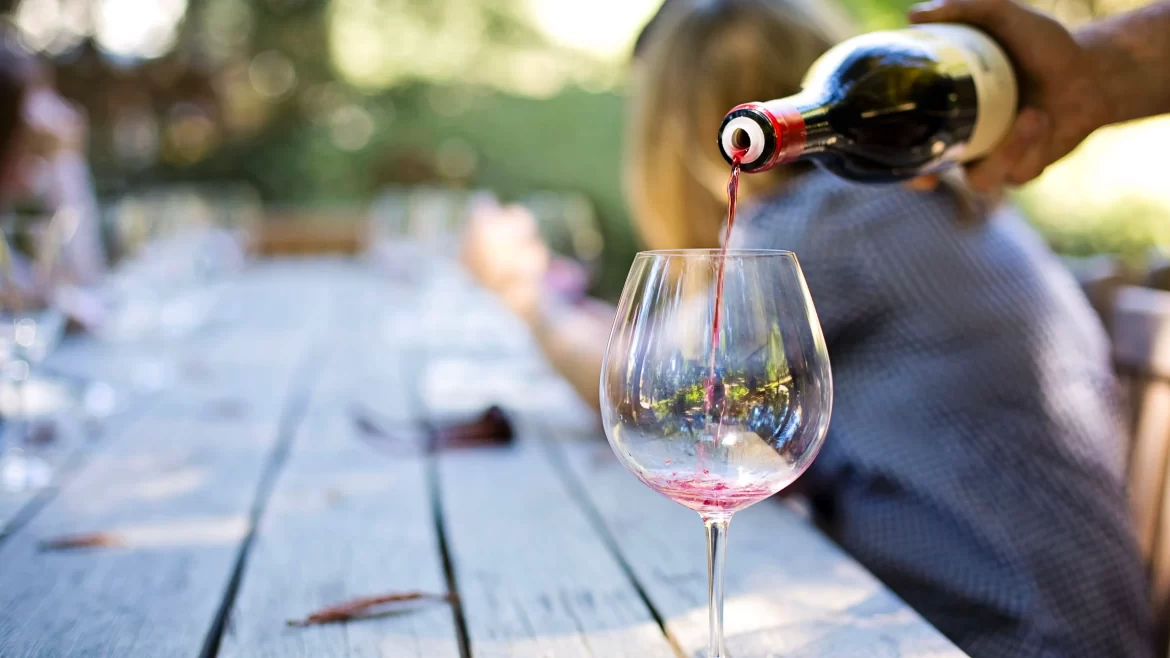 A red wine is poured into a glass on an outdoor wooden table.