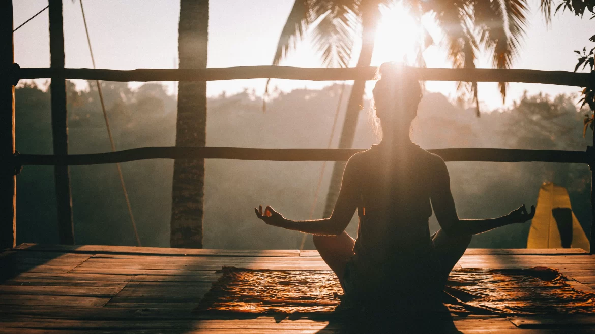 A woman sits in a seated yoga pose in front of a jungle backdrop.